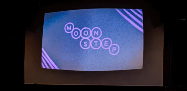 En una sala vacía y poco iluminada se está realizando una proyección de cine con las palabras "Moonstep" en la pantalla.