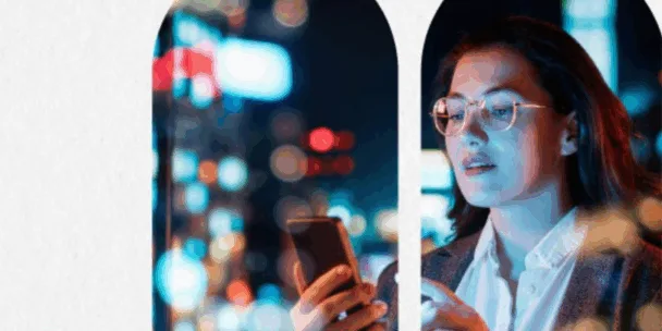 Gemini řekl: Obrázek osoby s brýlemi a tmavými vlasy, která se dívá na obrazovku chytrého telefonu, jenž osvětluje její obličej chladným modrým světlem. Jsou umístěni za řadou klenutých okenních rámů s výhledem na zářivou, rozmazanou noční městskou krajinu plnou barevných bokeh světel. Scéna evokuje moderní městskou atmosféru zaměřenou na technologie a konektivitu.